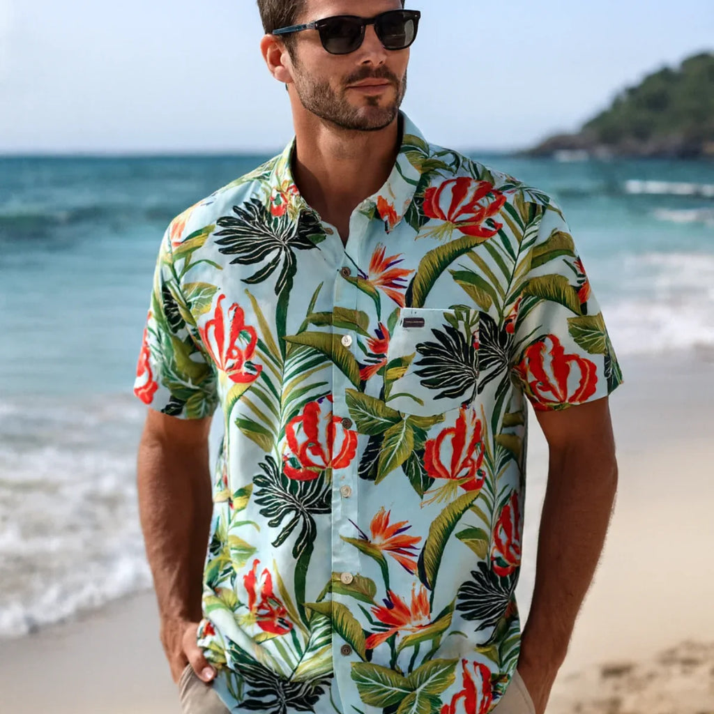 Homme portant une chemise polynésienne Tahiti Tropic à motifs tropicaux sur la plage - style décontracté chic avec lunettes de soleil