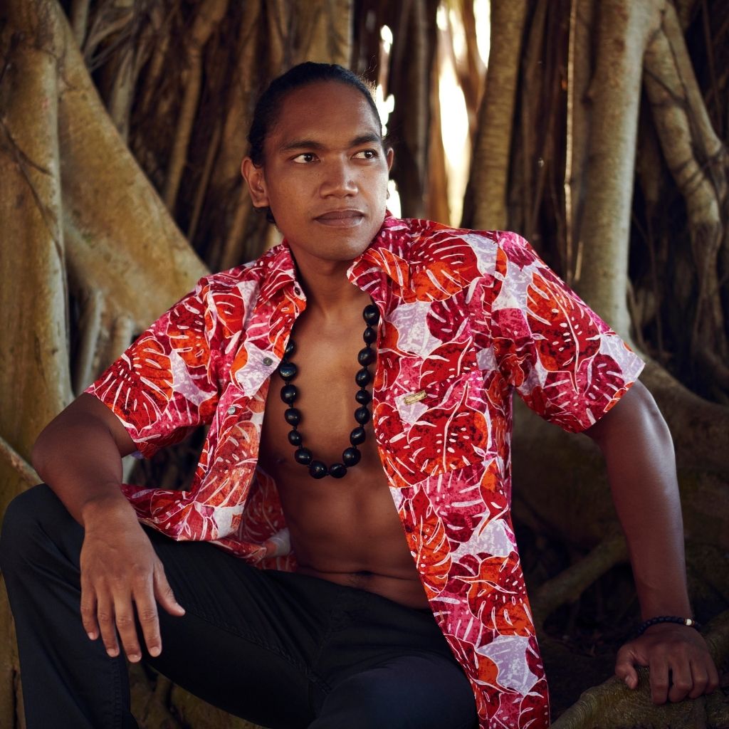 Jeune homme en chemise tahitienne en coton Terii Mahana monstera rouge, logo et boutons en nacre de Tahiti