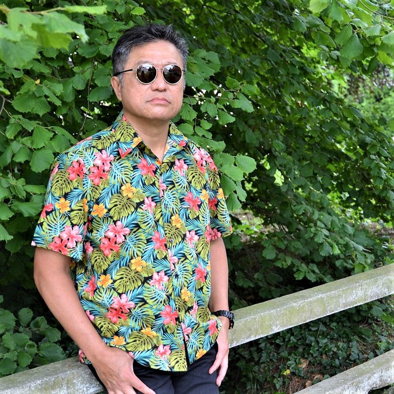 Homme portant chemise tahitienne hibiscus rose et jaune sur fond noir. Chemise en coton manches courtes, tissu tahitien et boutons en nacre. Edition limitée